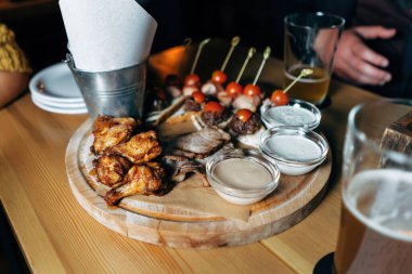 Ahşap arka planda soğuk bira, soslar ve aperatiflerle servis edilen tavuk kanatları. Gerçek bira barı..