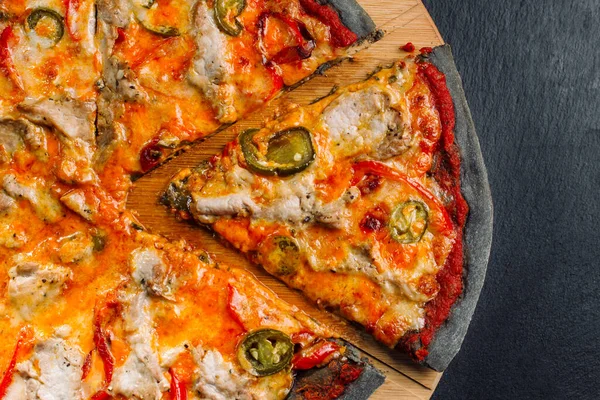 Pizza s paprikou jalapeno, sušenými rajčaty a kuřecími prsíčky na černém těstě. — Stock fotografie