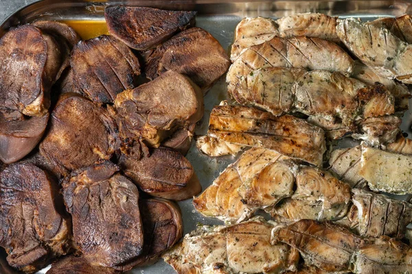 Sturgeon steaks baked on charcoal, laid out on a baking sheet on one side and tongues on the other side.