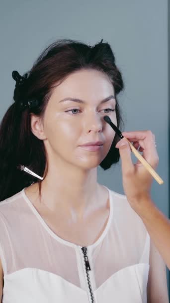 Eine junge Frau mit schlechter Haut lässt sich von einem professionellen Stylisten schminken. Den Ton auf das Gesicht auftragen. — Stockvideo