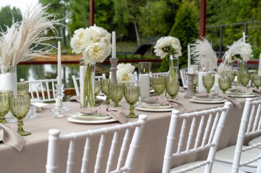 Süslü düğün masası, beyaz şakayıklar ve tüyler. Chiavari sandalyeleri masada..