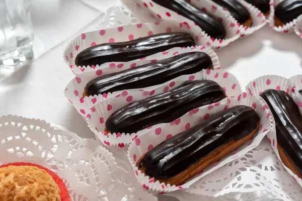 Chocolate coated eclairs. Several cakes are laid out on napkins. Clouse-up.