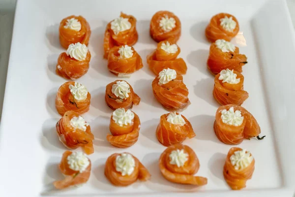 Rolls of salmon with cream cheese close-up on the table horizontal, diagonal composition on a beautiful white plate. — Stock Photo, Image