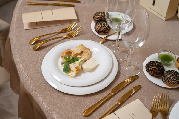 Шикарные и элегантные, позолоченные столовые приборы и белые тарелки. На тарелке несколько видов сыра. — стоковое фото