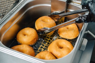 Donutlar yağda kızarıyor. Geleneksel donut hazırlama, altı yuvarlak yağlı çörek. Aşçı yağdan bir çörek alıyor..
