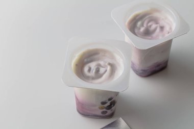 Lezzetli tatlı ya da beyaz arka planda izole edilmiş beyaz yaban mersinli yoğurt kremalı plastik kaplar.