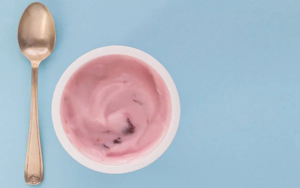 Yogurt cup with pink strawberry yoghurt isolated on baby blue background with copy space - selective focus photo