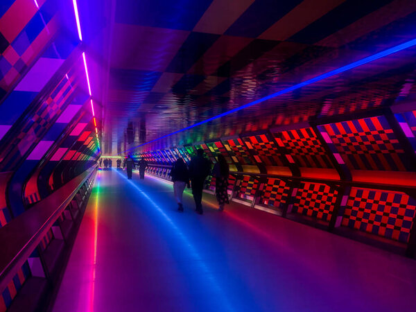 Colourful pedestrian tunnel at Canary Wharf in London. You can see shapes of people in the distance at the other end of the tunnel.