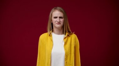 Kız elleriyle kulaklarını kapatıyor, çok gürültülü, gergin, beyaz bir tişört ve sarı bir gömlek giyiyor, arka plan kırmızı.