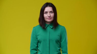 Kız gözlük takıyor ve gülümsüyor, esmer, kısa saçlı, yeşil gömlekli, arka plan sarı.