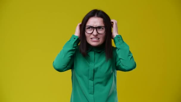 女人全身发痒 她很生气 穿着绿色的衬衫 戴着眼镜 背景是黄色的 — 图库视频影像
