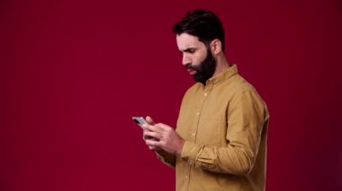Adam yemi kaydırıyor ve hoş bir şekilde şaşırıyor, koyu saçlı, sakallı, kahverengi gömlek giyiyor, arka plan kırmızı.