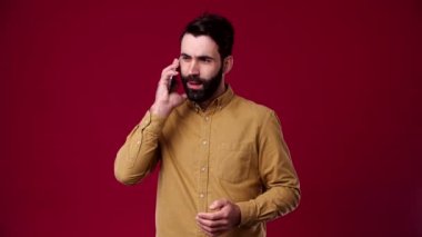 Köylüye bir telefon geldi ve iyi haber verildi, hemen olumlu bir ruh hali vardı, sakallı, siyah saçlı, kahverengi gömlekli, arka planı kırmızı.