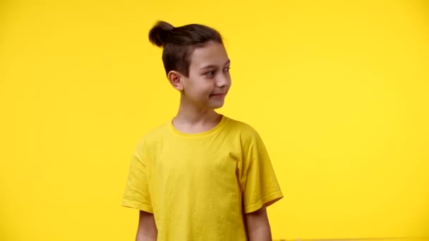男孩静静地展示了相机 黑头发 留着马尾辫 穿着一件黄色衬衫 背景是黄色的 — 图库视频影像