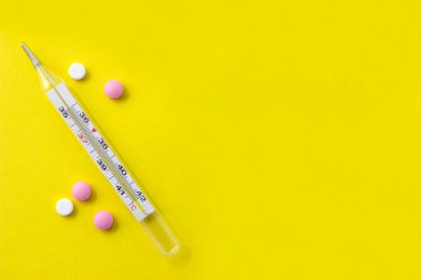 Tıbbi termometre ve sarı arka plandaki haplar tasarımınız için..