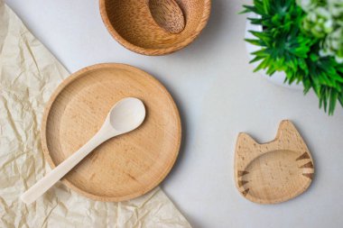 Mutfak masasındaki ahşap çatal bıçaklar. Yuvarlak tahta tabaklar, kedi şeklinde alışılmadık bir tabak, tahta kaşık, yeşil bir bitki. Servis yapma, yemek pişirme, içsel detaylar..