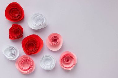 Beyaz, pembe ve kırmızı origami gülleri açık arkaplana saçılmıştır. Tasarımınız için yer