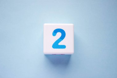Mavi arka planda mavi bir 2 numaralı beyaz plastik küpün yakın plan fotoğrafı. Fotoğrafın ortasındaki nesne.