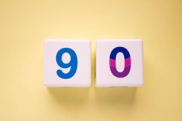 Close-up photo of a white plastic cubes with a colorful number 90 on a yellow background. Object in the center of the photo