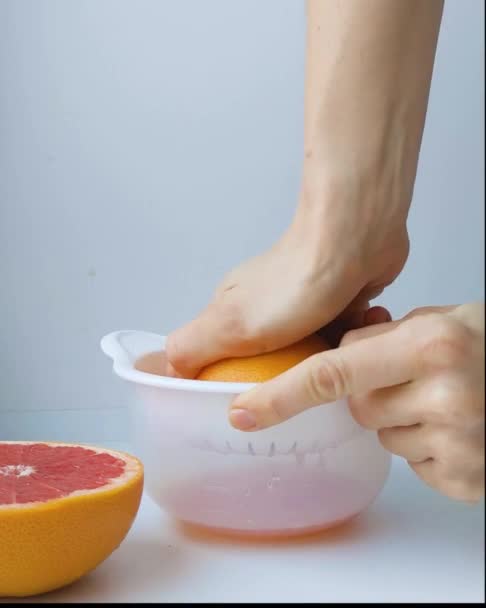 Human hand squeezing fresh grapefruit juice process, close up, front view — Stock video