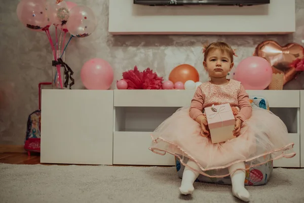 2 year baby girl in pink dress with her first birthday cake, happy birthday card,a cute little girl celebrates her first birthday surrounded by gifts