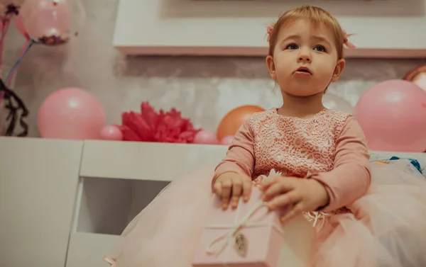 2 year baby girl in pink dress with her first birthday cake, happy birthday card,a cute little girl celebrates her first birthday surrounded by gifts