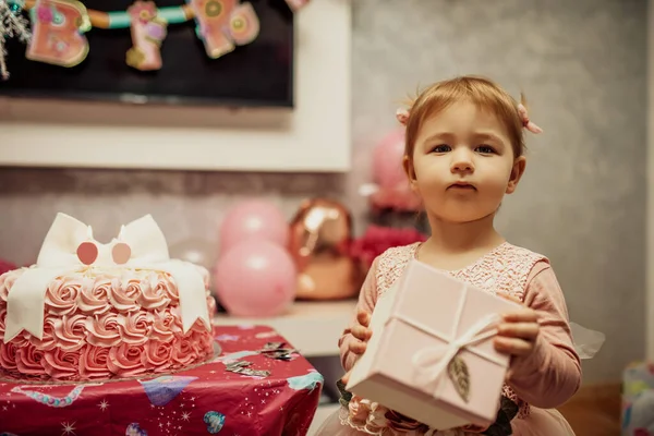 2 year baby girl in pink dress with her first birthday cake, happy birthday card,a cute little girl celebrates her first birthday surrounded by gifts