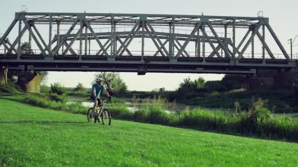 El tipo monta una bicicleta en el césped en un hermoso paisaje — Vídeos de Stock