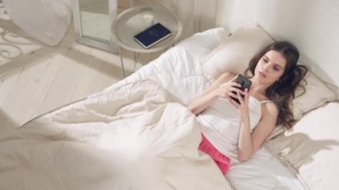 Genç kız yatakta akıllı telefona bakıyor..