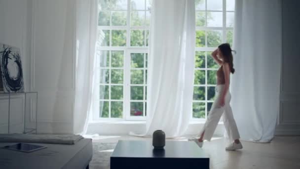 Ung flicka i en vacker interiör i vardagsrummet tittar på stora fönster — Stockvideo