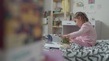 Bebek odasında yatağın üstünde kitap okuyan küçük bir kız.. 