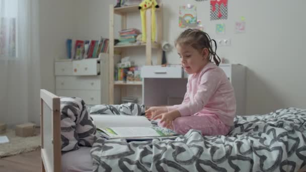 Blank meisje leest een boek op het bed in de kinderkamer. — Stockvideo