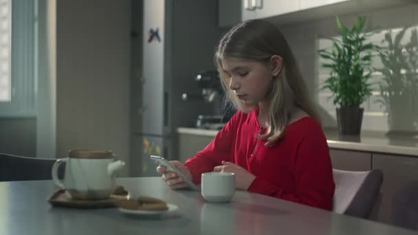Hermosa adolescente sentada en la cocina en la mesa con una taza de té — Vídeo de stock