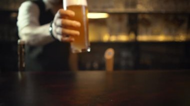Barmen barda müşteriye servis yapıyor, yarım litre bira koyuyor. Bir kupa filtresiz bira..