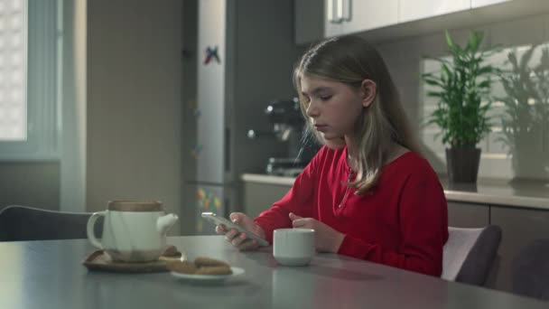 Adolescente chica mira el teléfono mientras está sentado en la cocina. — Vídeo de stock