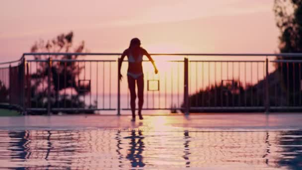 Tiener duikt in het zwembad bij zonsondergang. Meisje springen in het water in slow motion — Stockvideo