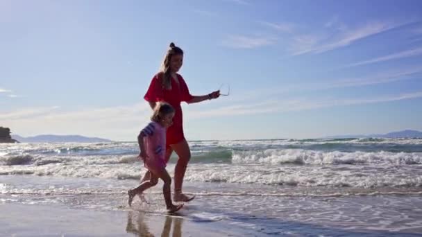 Giornata estiva sulla spiaggia vicino all'oceano. Donna con bambina cammina sulla costa della spiaggia. — Video Stock