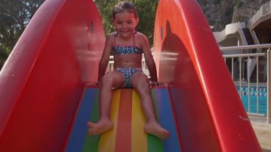 Küçük kız kaydırağın içine giriyor. Havuzda su sıçratan çocuk