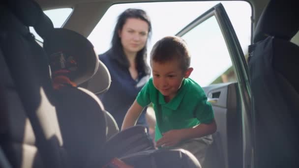 少年は車の座席に入る。ママは車の座席で子供を固定してる — ストック動画