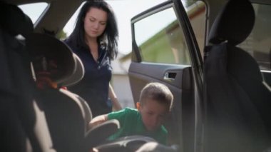 Çocuk çocuk araba koltuğuna oturur ve annesi emniyet kemerini bağlar.. 