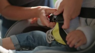 Çocuk oto koltuğuna emniyet kemeri takan kadın ellerinin yakın çekimi.