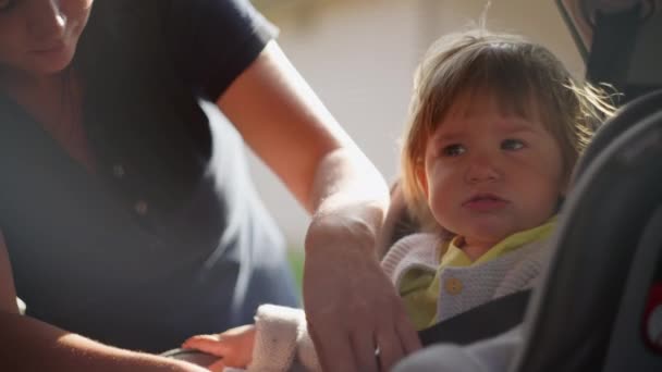 A woman fastens a child sitting in a child car seat with seat belts. — Vídeos de Stock