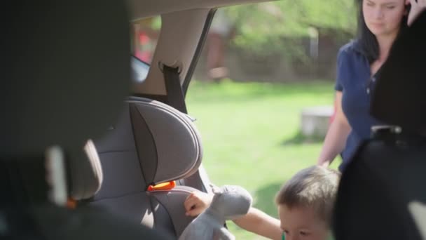 Mom puts and fastens her son in a child seat in the car. — Vídeos de Stock