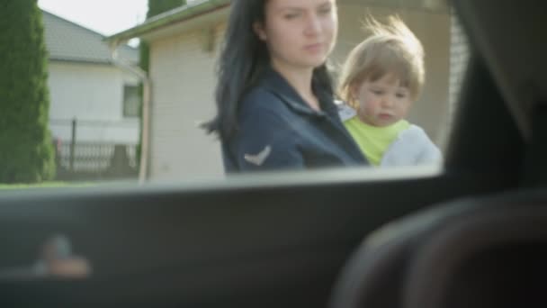 Mom carries her daughter in her car and puts her in a child car seat. — Stockvideo