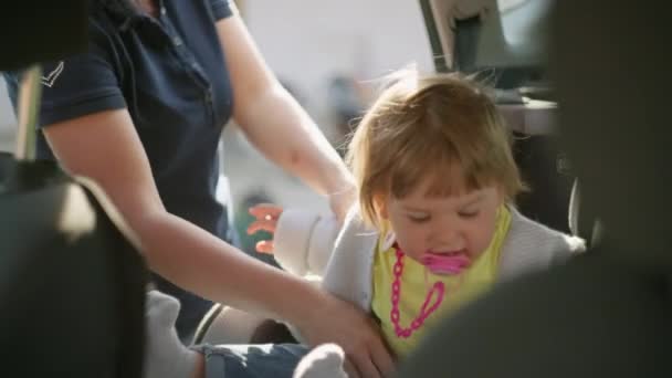 Mãe coloca sua filha em um assento de carro de bebê. — Vídeo de Stock