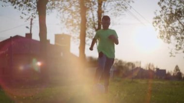 Güneşli havada kılıçla oynayan bir çocuk. Çocuk futbolcu topa ayağıyla öncülük ediyor..