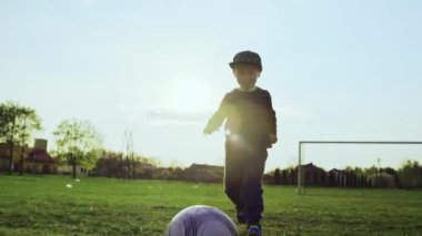 Çocuk topa vuruyor. Bir çocuk arkadaşlarıyla stadyumda futbol oynuyor. gün batımı ve spor yapan insanlar.