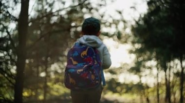 Çocuk sırtında bir sırt çantasıyla ormanda yürüyor. Çocuk gün batımında manzara yürüyüşü yapıyor. Dağlara aktif tatil gezisi.