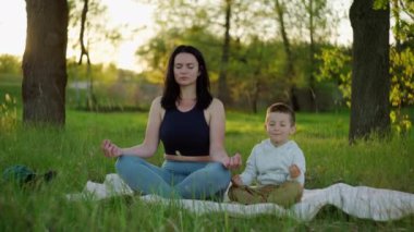 Anne ve oğlu doğayla iç içe. Yaşam tarzı anne ve çocuk, parktaki bir ağacın altında meditasyon yapıyorlar..