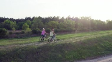 Yaşam tarzı eril manzara. Doğada bisiklet süren iki kız. Aktif eğlence ve takım çalışması, anne ve kız gün batımında ağaçlarla ve patikalarla parkta bisiklet sürüyor..